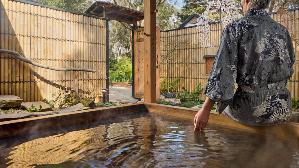 A guest in yukata trailing a hand in the private outdoor hinoki bath at Shizuka Ryokan