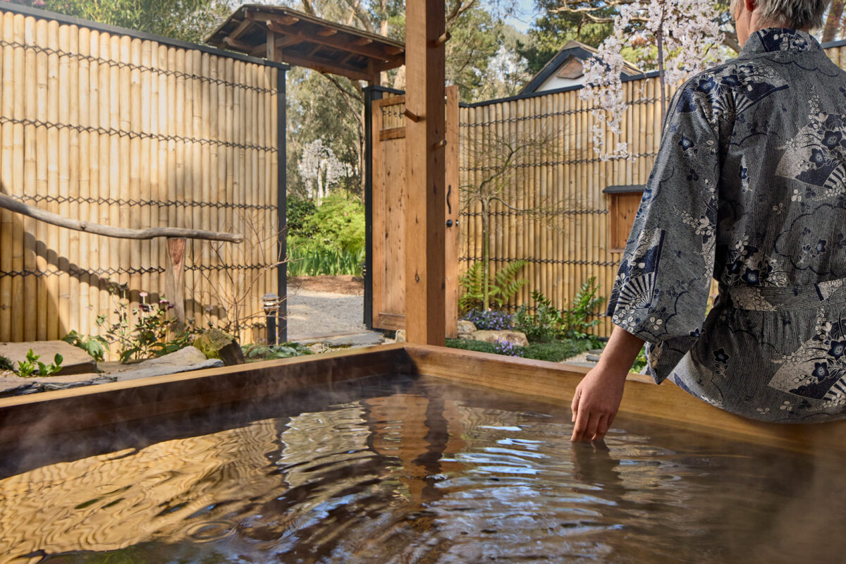 A guest in yukata trailing a hand in the outdoor hinoki bath at Shizuka Ryokan